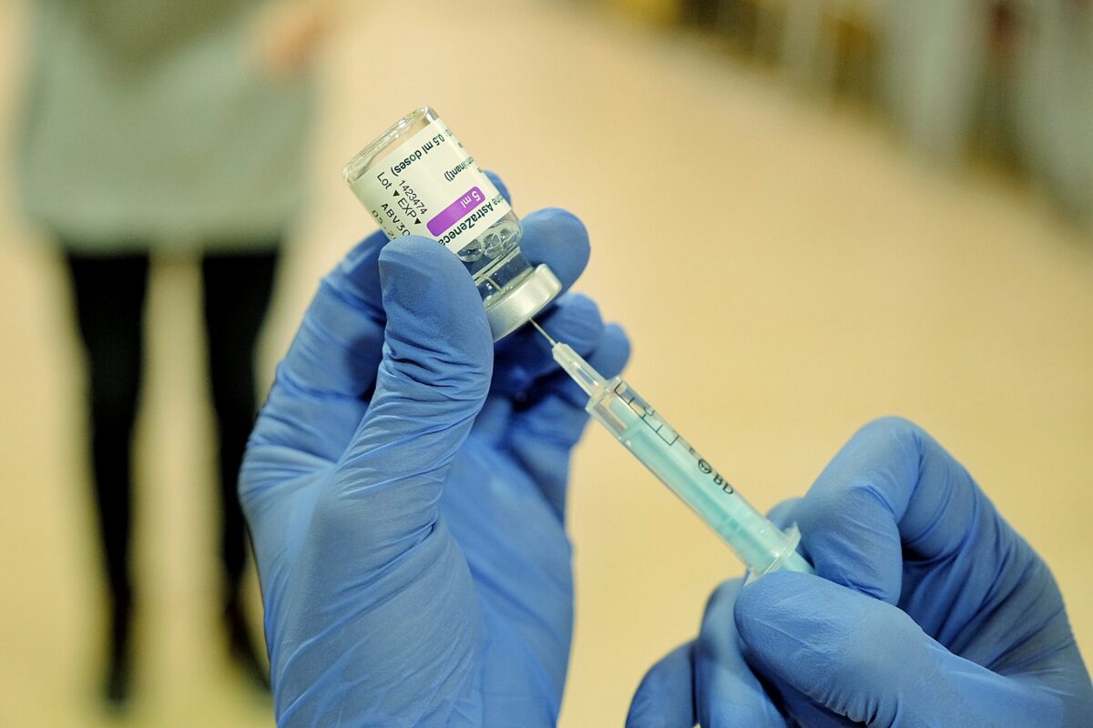 Gloved hands drawing vaccine from a small vial with a syringe.