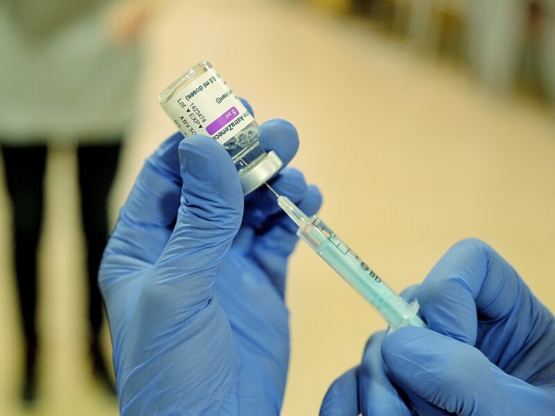 Gloved hands drawing vaccine from a small vial with a syringe.