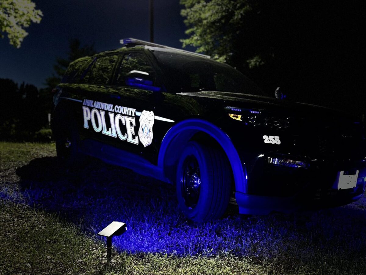 Black police SUV parked at night with blue lights illuminating the grass.