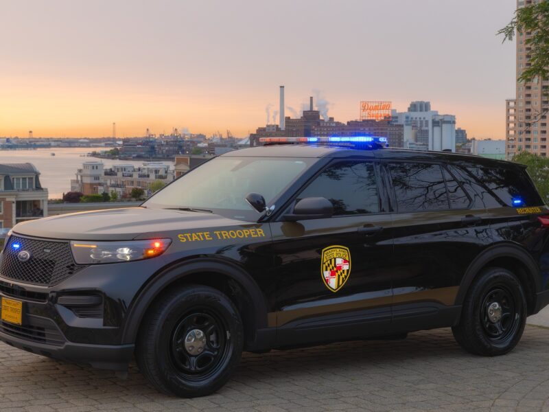 Maryland state trooper SUV parked at a waterfront overlook at sunset with blue lights flashing.