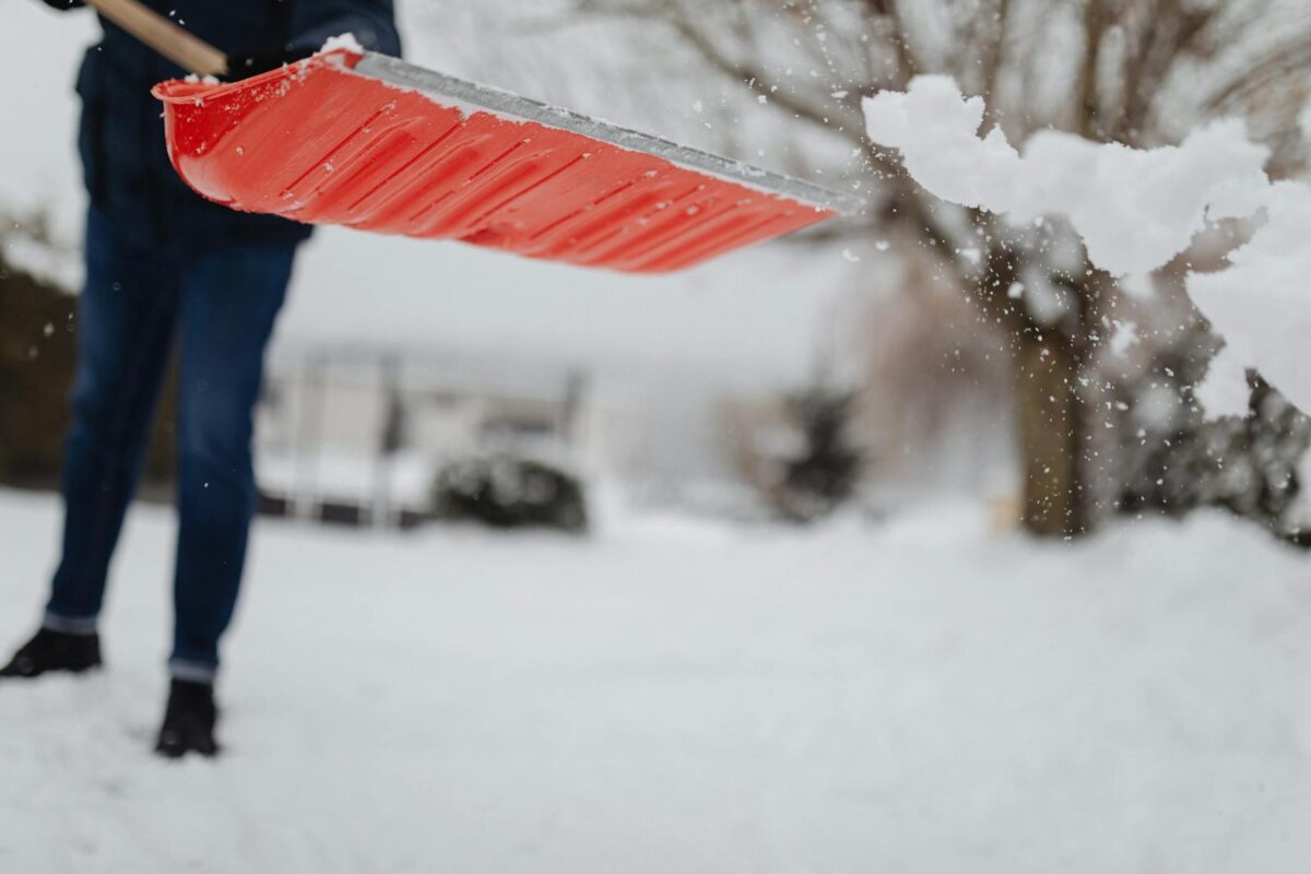 A person shovels snow with a bright red shovel during a winter day.