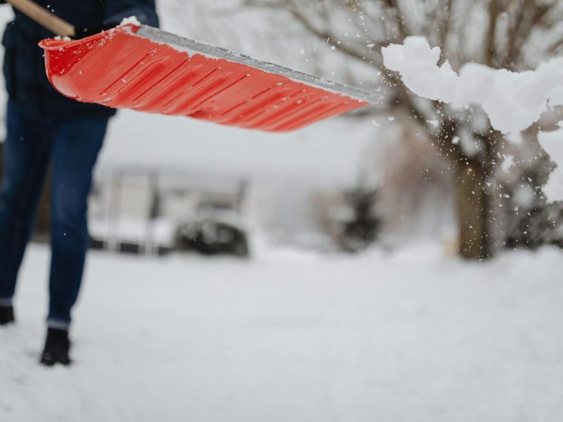 A person shovels snow with a bright red shovel during a winter day.