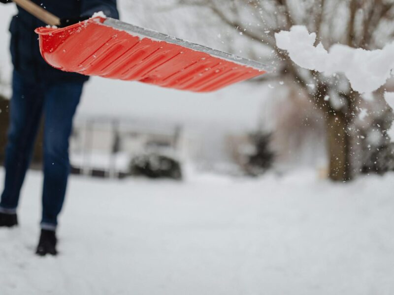 A person shovels snow with a bright red shovel during a winter day.