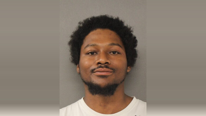Mugshot-style portrait of a man against a plain gray background wearing a white shirt.