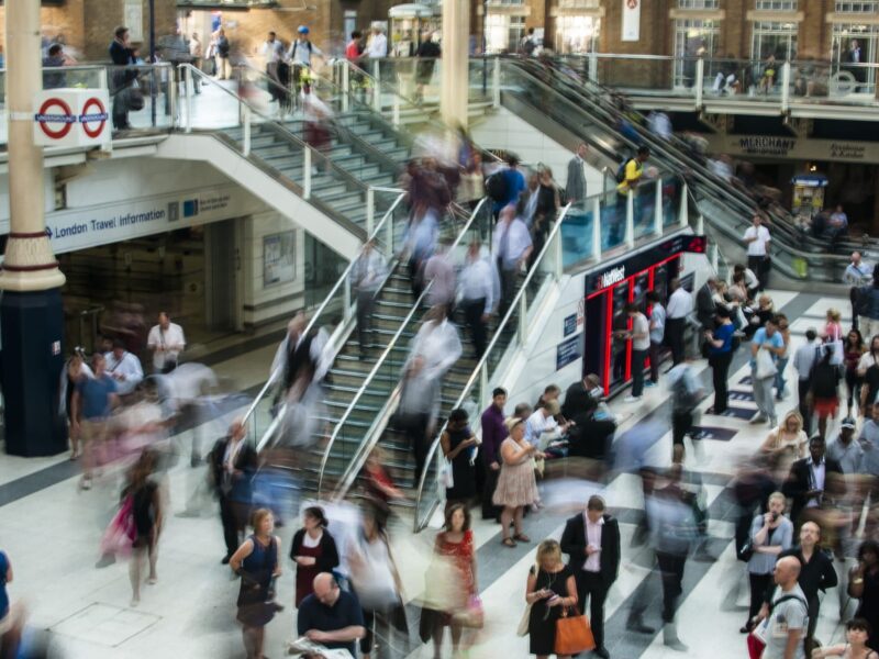 Crowded indoor train station concourse with blurred commuters on escalators and stairs.