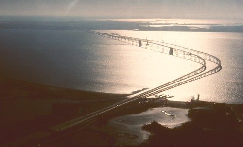 Curving bridge spans sunlit water at dusk over a coastal bay.