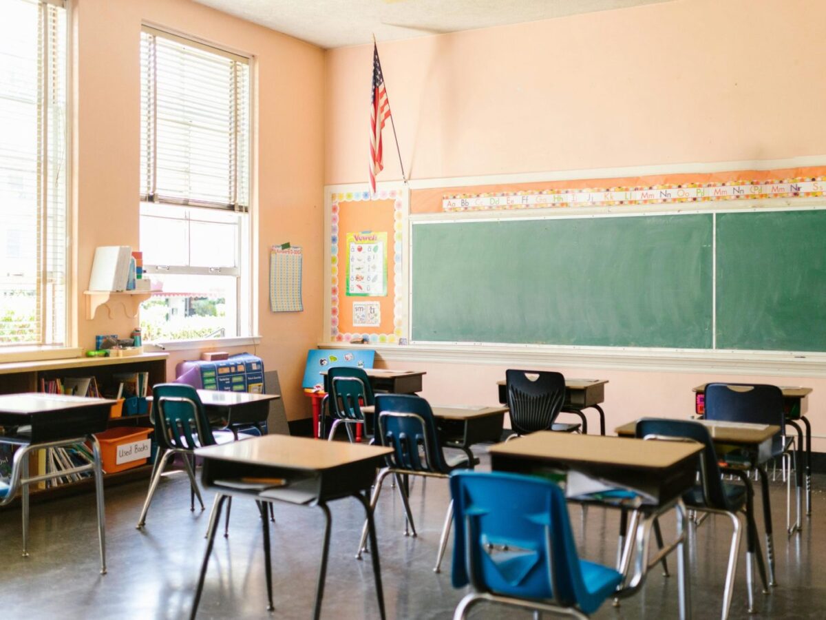 An inviting, sunlit classroom with empty desks and an American flag, ready for students.