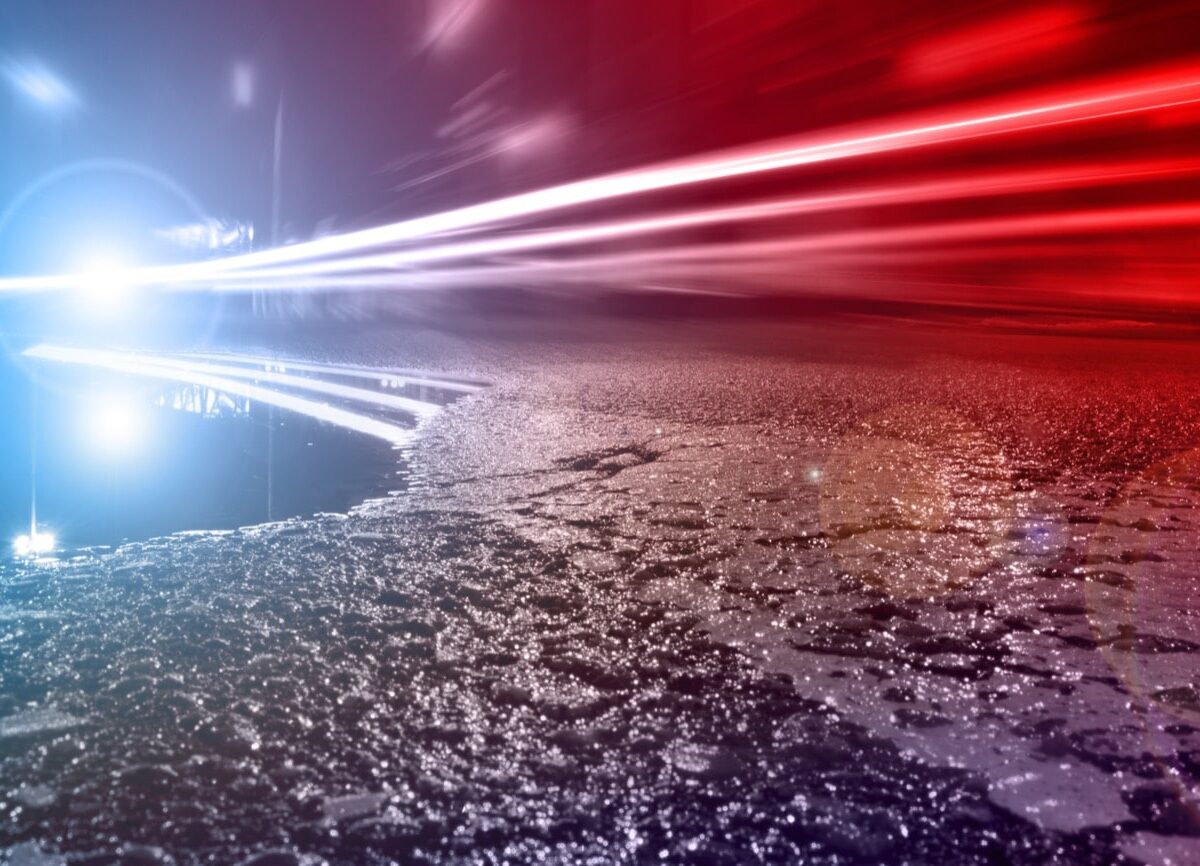 Blue and red light streaks race over a wet road at night with a bright glare on the left.