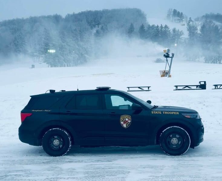 State trooper SUV parked on a snowy landscape with foggy hills and trees in the background.