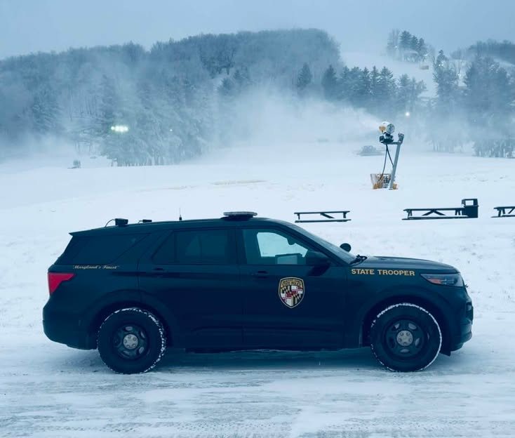 State trooper SUV parked on a snowy landscape with foggy hills and trees in the background.