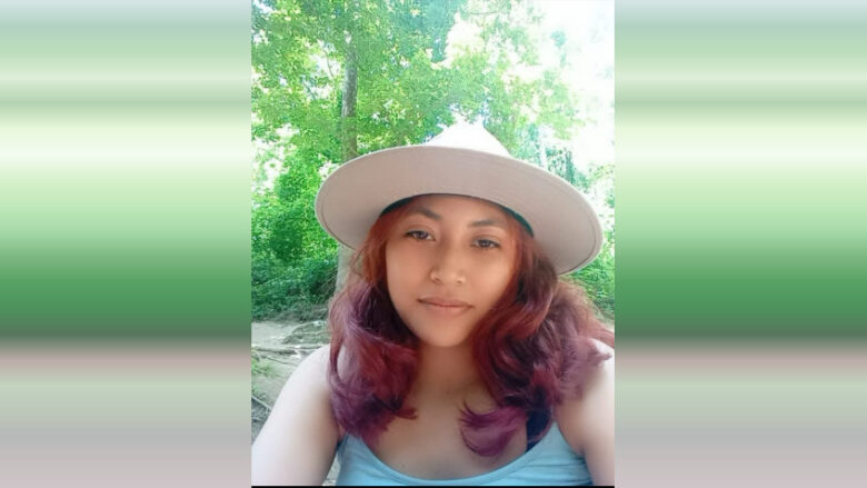 Woman in a wide-brim hat taking a selfie outdoors in a lush green setting.