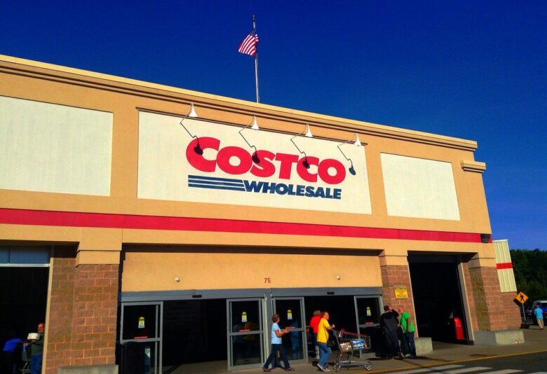 Costco Wholesale storefront with shoppers entering under a clear blue sky.