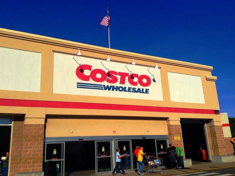 Costco Wholesale storefront with shoppers entering under a clear blue sky.