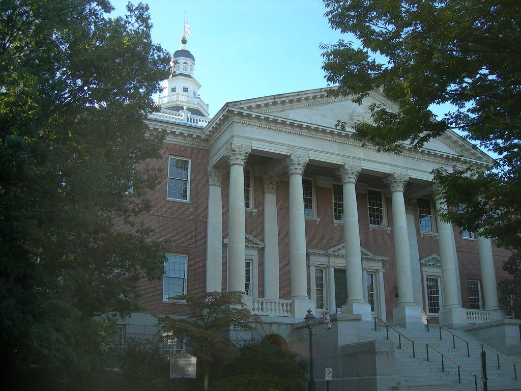 Historic neoclassical brick building with tall white columns and a stepped entrance framed by trees.