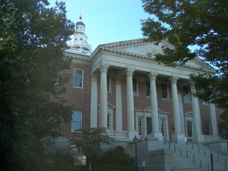 Historic neoclassical brick building with tall white columns and a stepped entrance framed by trees.
