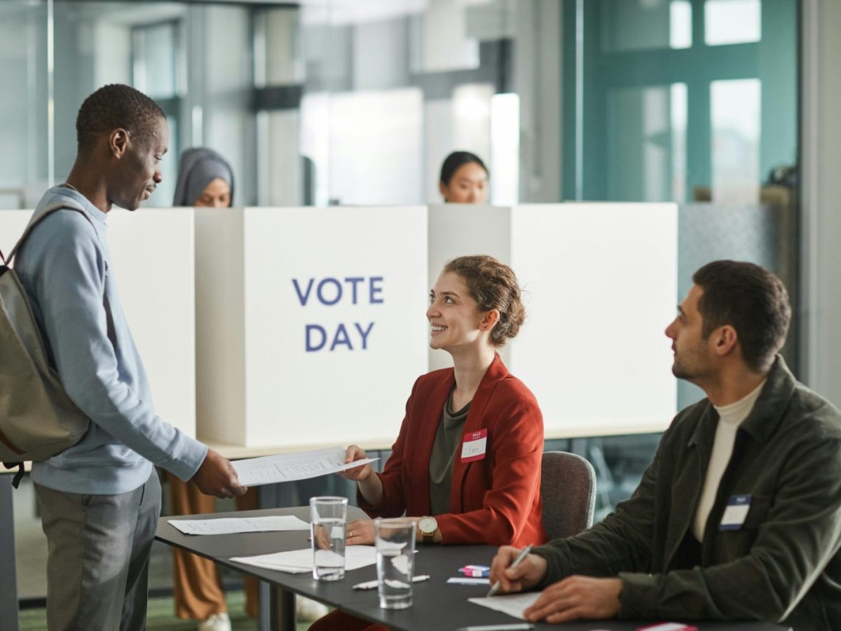Diverse group of voters and officials at an indoor polling station on voting day.