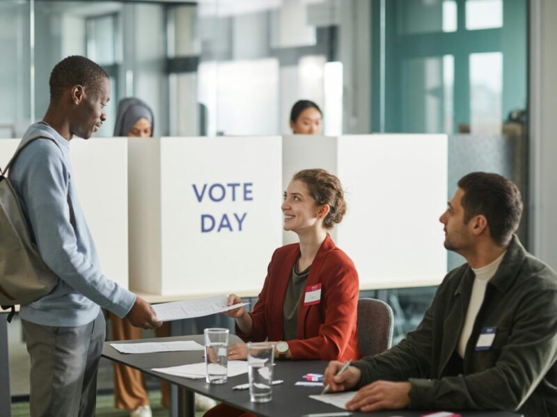 Diverse group of voters and officials at an indoor polling station on voting day.