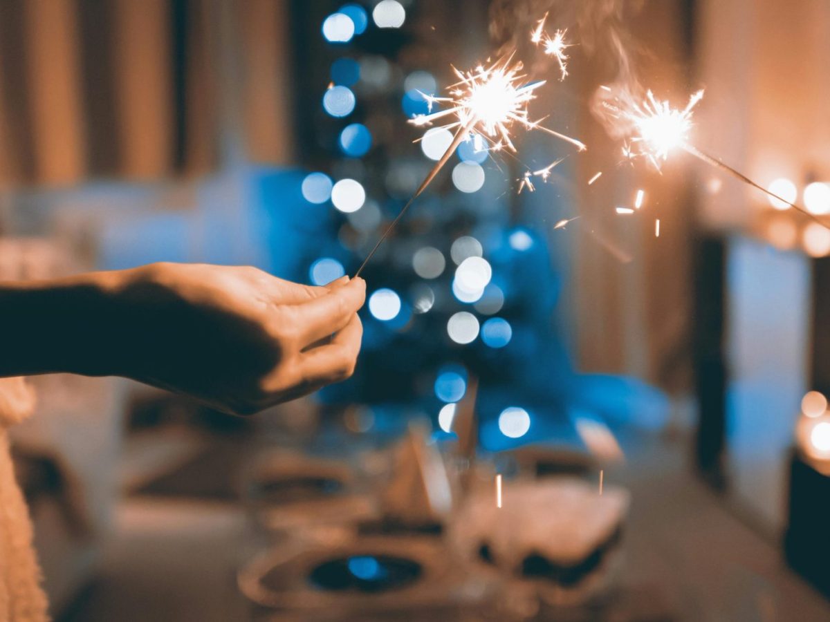 Hands holding sparklers in a festive indoor setting with blurred lights and bokeh effect.