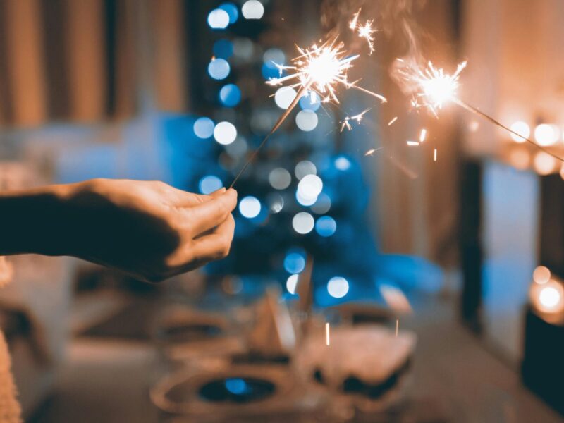 Hands holding sparklers in a festive indoor setting with blurred lights and bokeh effect.