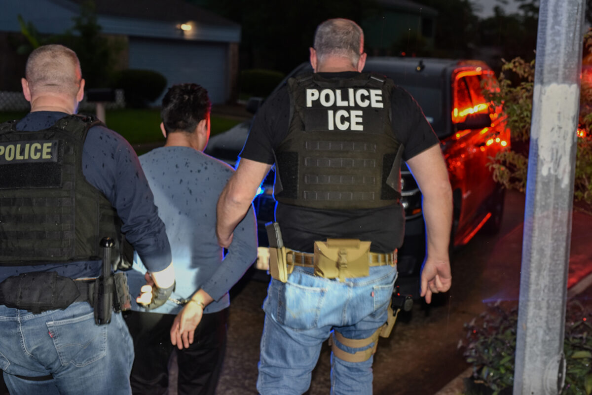 Police officers escort a handcuffed man toward a vehicle at night