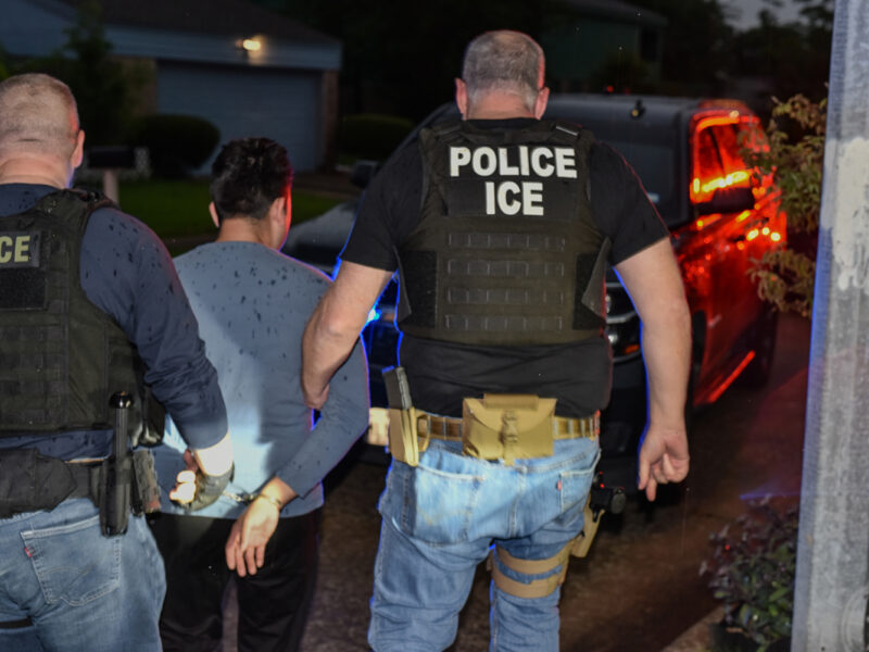 Police officers escort a handcuffed man toward a vehicle at night