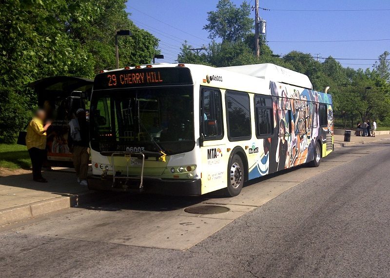 City bus stopped at a curb with passengers boarding on a tree-lined street.