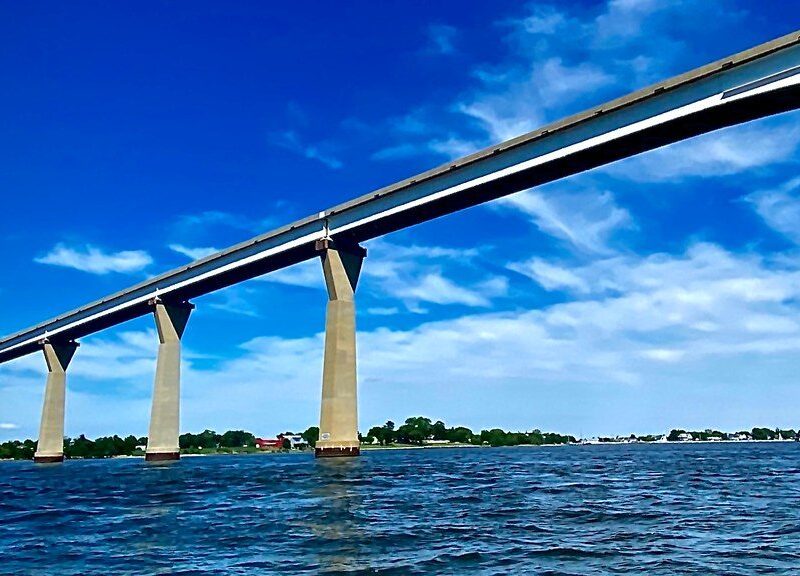 Long concrete bridge stretches across blue water under a bright sky with scattered clouds.