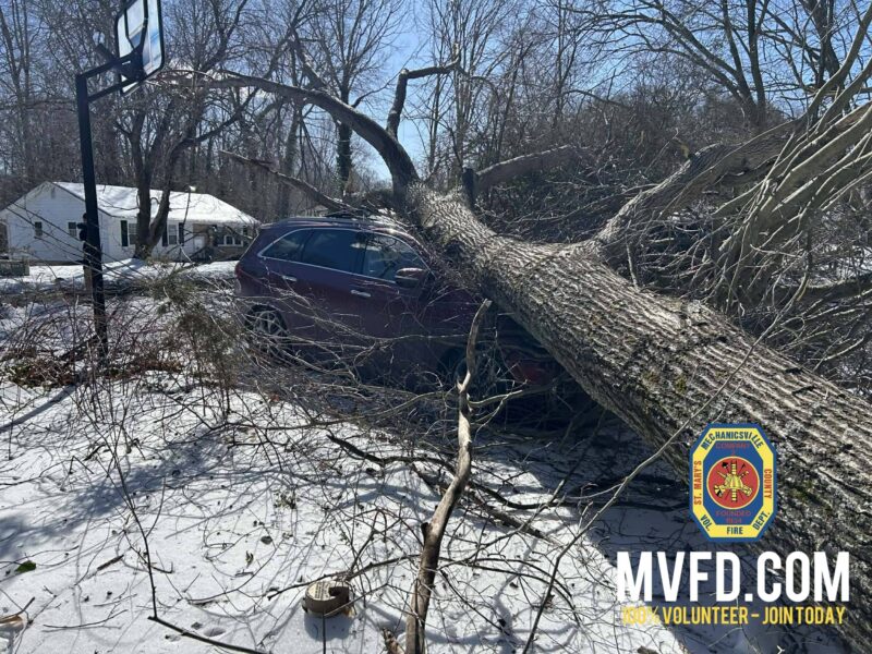 Fallen tree crushes a maroon SUV in a snowy yard near a house.
