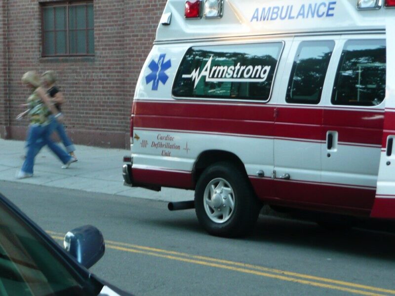 Armstrong ambulance parked on a city street beside a sidewalk and brick building.