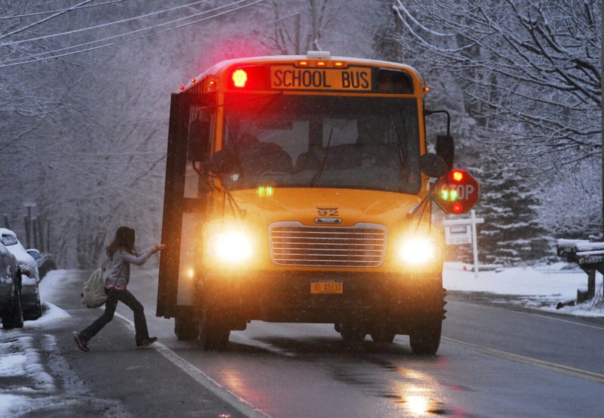 A school bus on a snowy road with a child boarding in winter conditions.