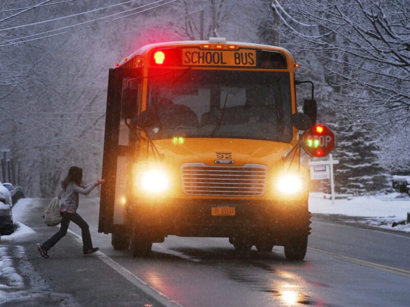 A school bus on a snowy road with a child boarding in winter conditions.