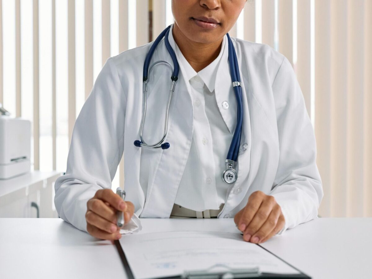 A focused doctor with stethoscope recording patient details in an office setting.