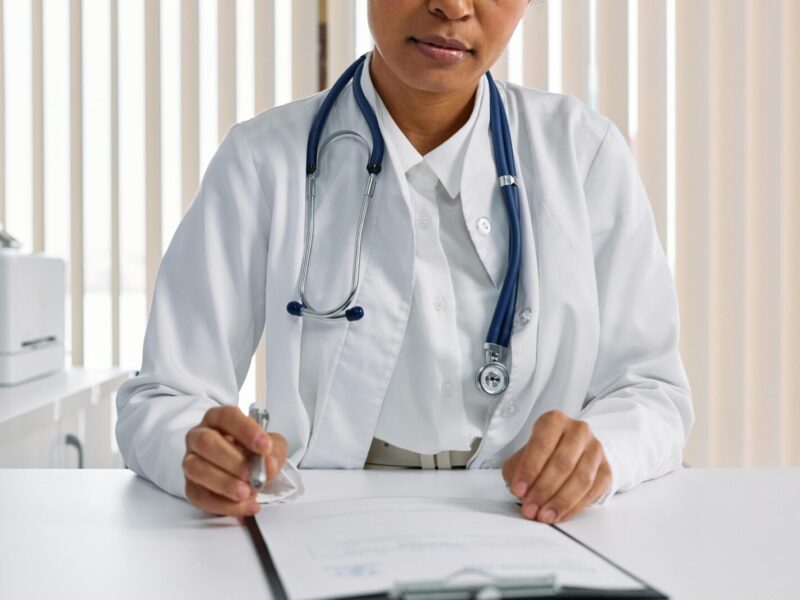 A focused doctor with stethoscope recording patient details in an office setting.