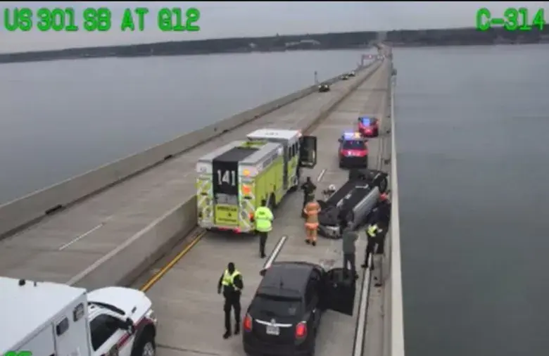 Police and rescue workers attend a truck crash on a long bridge over water.