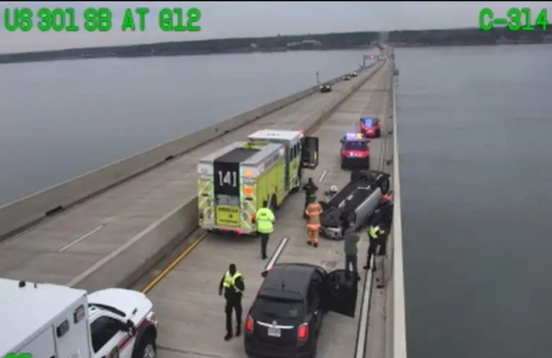 Police and rescue workers attend a truck crash on a long bridge over water.