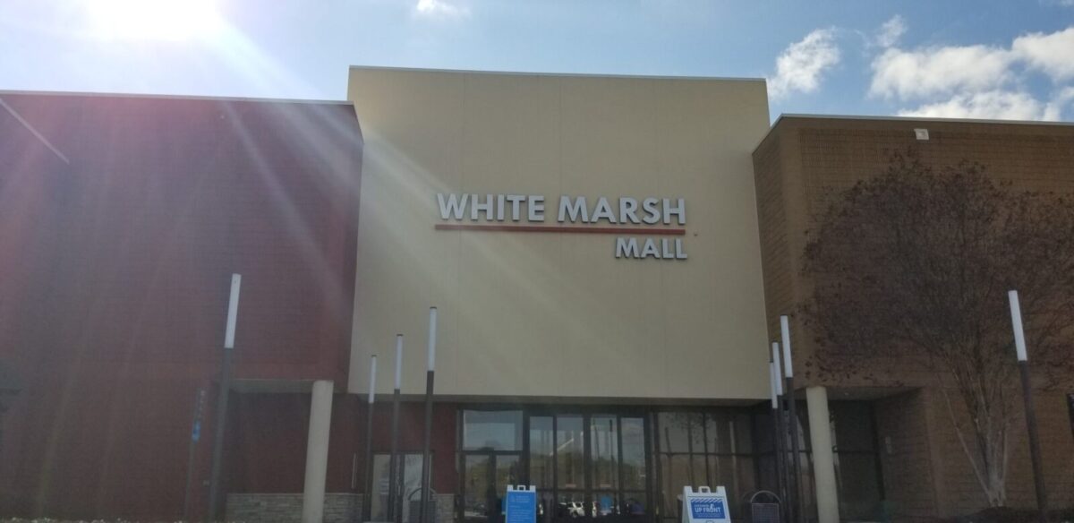 Exterior of White Marsh Mall under a bright blue sky with sun glare.