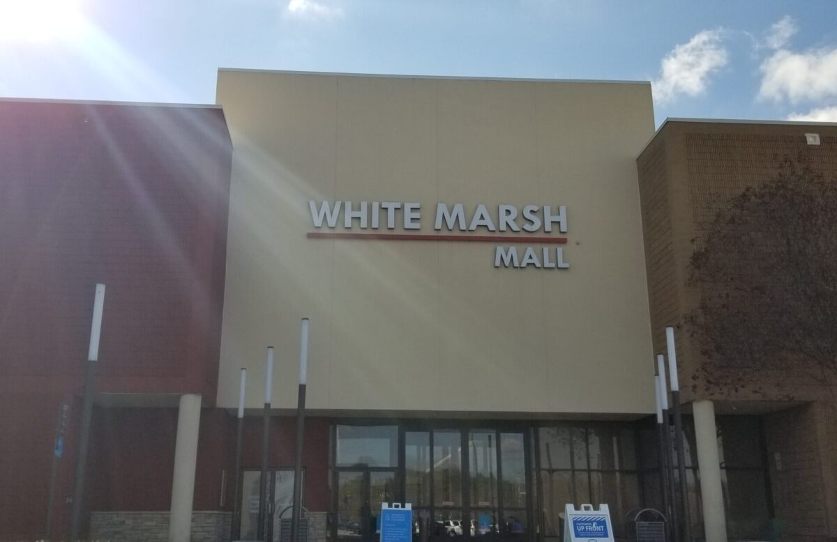 Exterior of White Marsh Mall under a bright blue sky with sun glare.