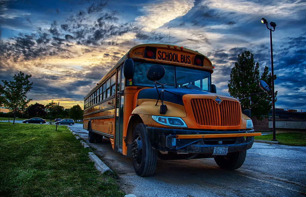Yellow school bus parked on a road at dusk under a dramatic cloudy sky.