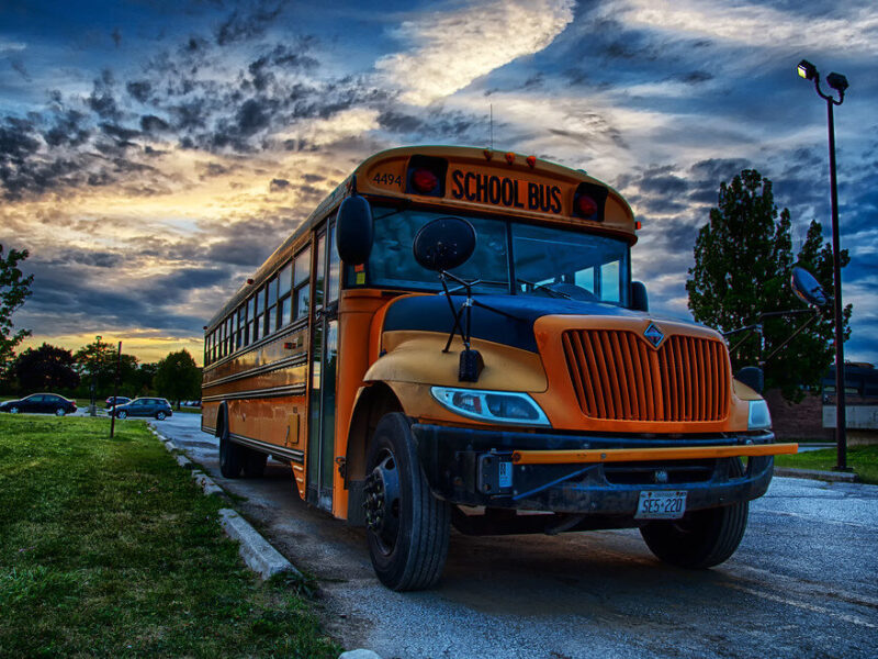Yellow school bus parked on a road at dusk under a dramatic cloudy sky.