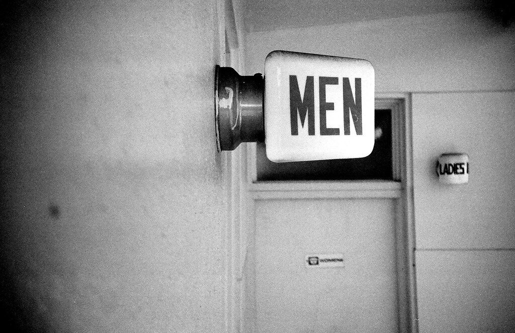 Men’s restroom sign on a wall in a black-and-white hallway.