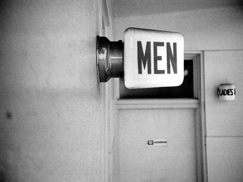 Men’s restroom sign on a wall in a black-and-white hallway.