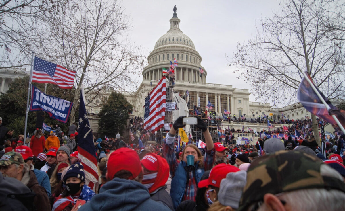 Crowd of protesters with Trump flags gathered outside the U.S. Capitol on an overcast day.