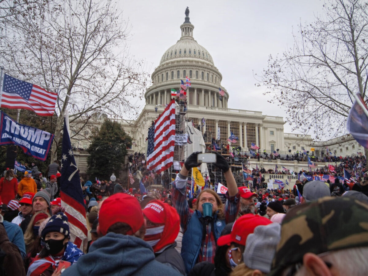 Crowd of protesters with Trump flags gathered outside the U.S. Capitol on an overcast day.