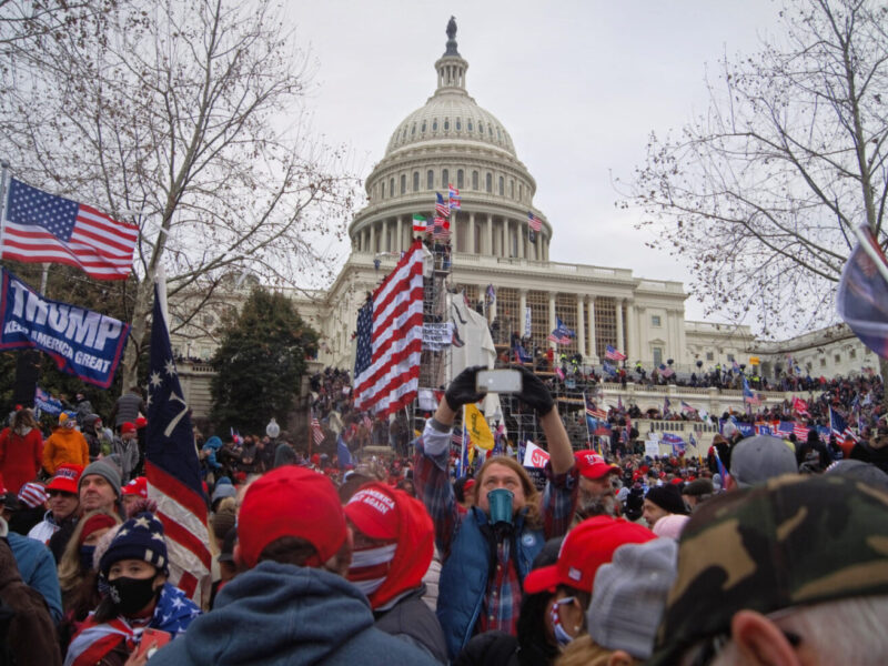 Crowd of protesters with Trump flags gathered outside the U.S. Capitol on an overcast day.
