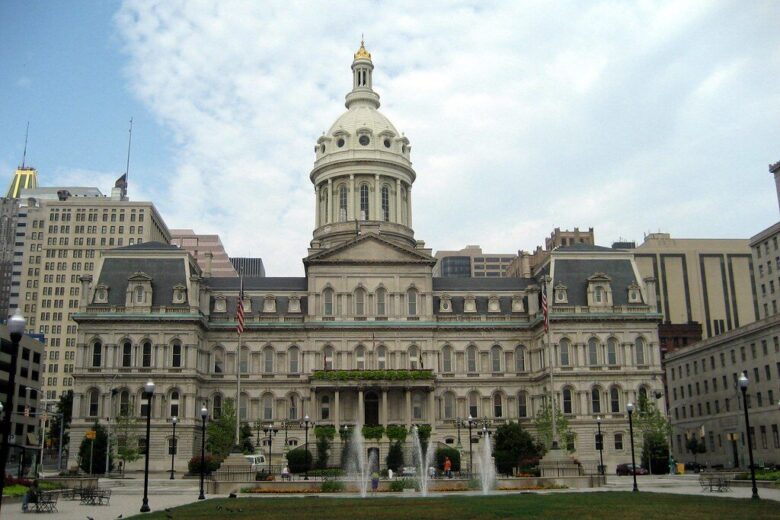 Historic civic building with a central dome and fountain in front under a cloudy sky.