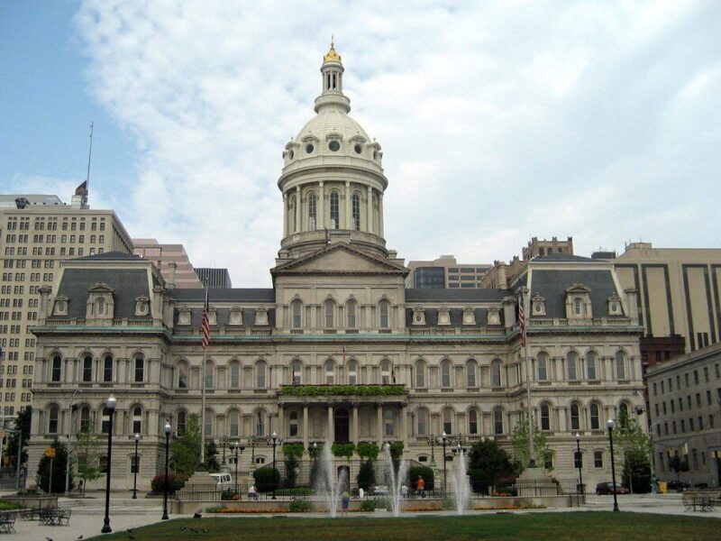 Historic civic building with a central dome and fountain in front under a cloudy sky.