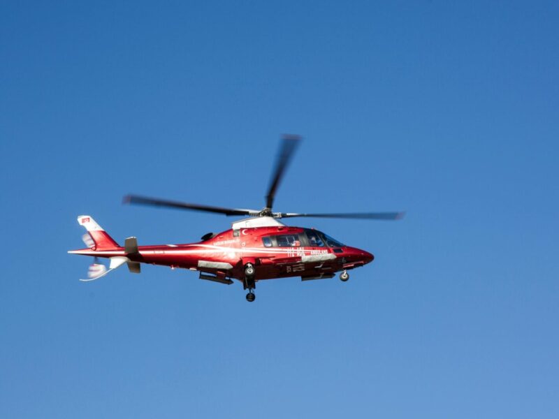 Red helicopter flying against clear blue sky, symbolizing emergency medical rescue.