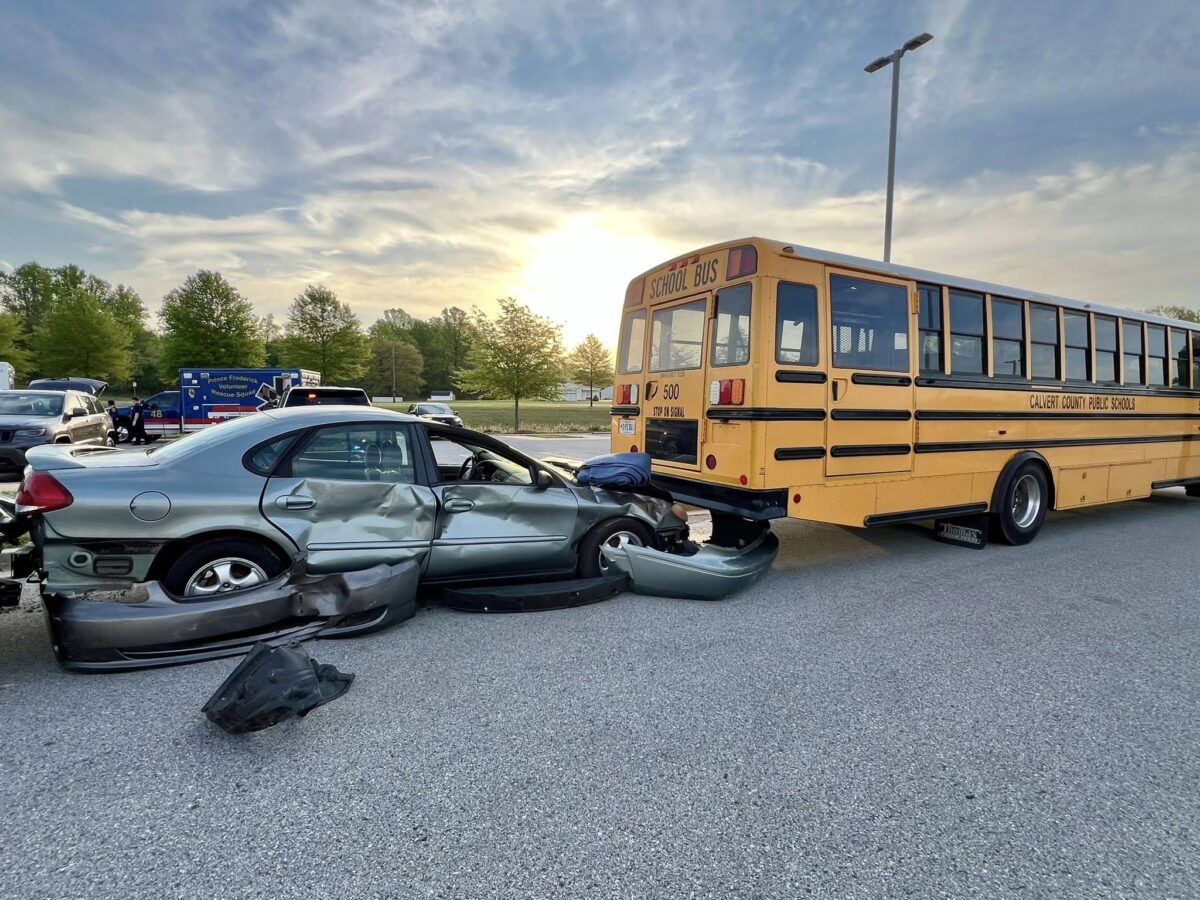 Damaged car and school bus after a collision on a roadway at sunset.