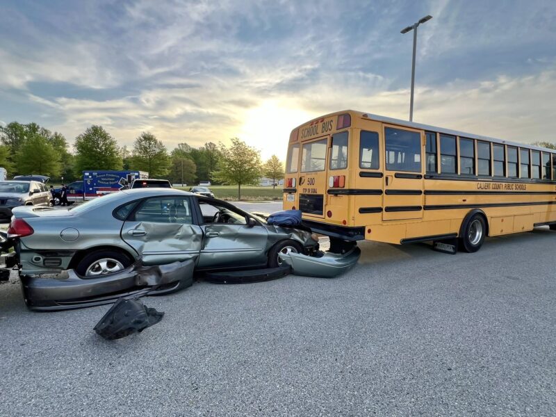 Damaged car and school bus after a collision on a roadway at sunset.