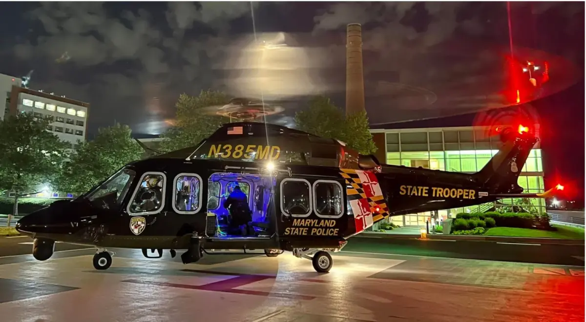 Maryland State Police helicopter parked at night with cabin lights glowing and rotor blur.